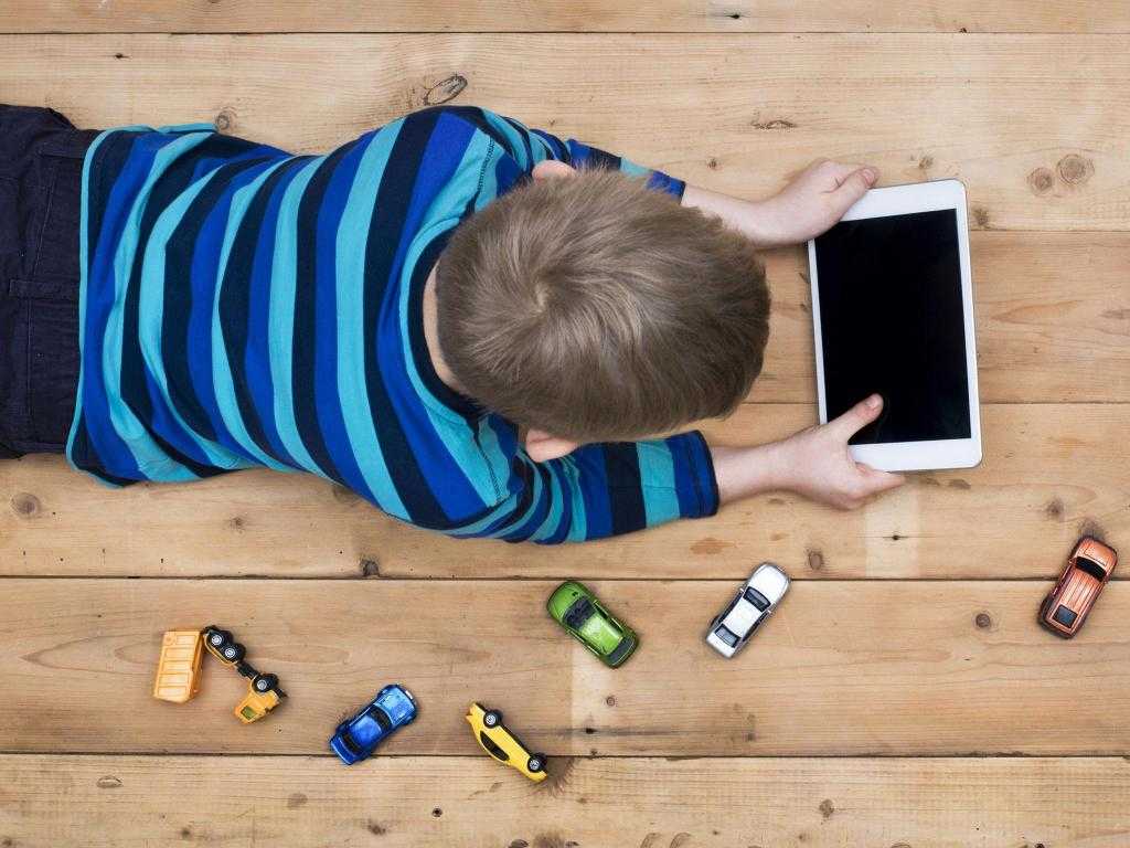 мальчик с планшетом возле игрушечных машинок